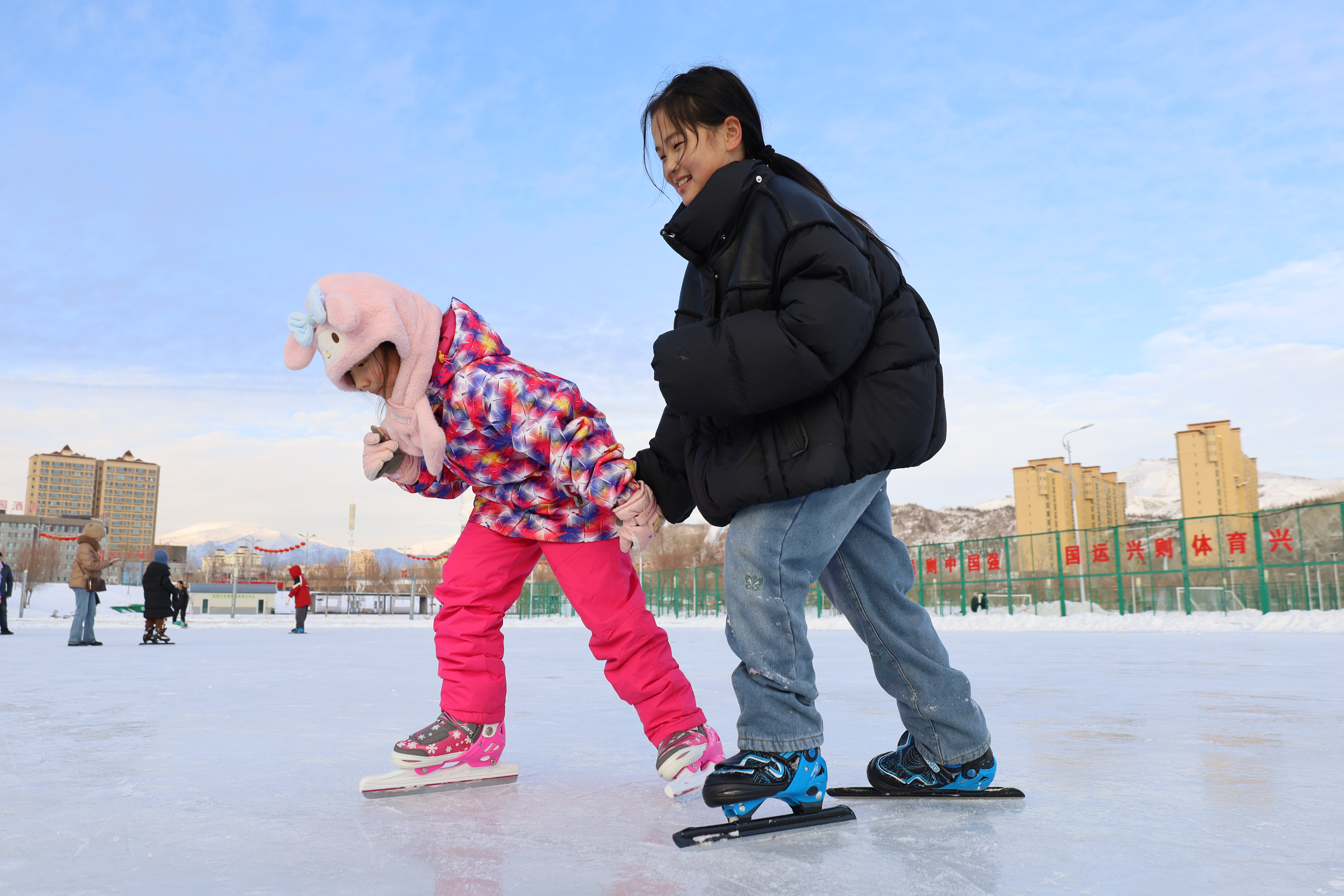 在滑冰场内，小朋友们手拉手滑冰，尽享冰雪运动的欢乐。